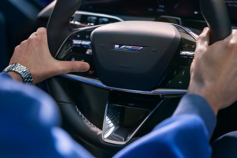 Close-up of a Man About to Press the V-Button on the 2026 OPTIQ-V Steering Wheel | Lima Cadillac in LIMA OH